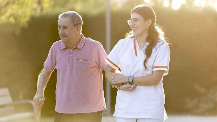 Una cuidadora pasea con un residente en verano.