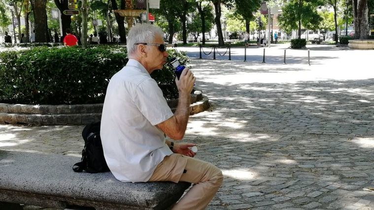 Hidratación, una persona mayor bebe agua en el parque.